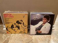 Two stacks of vinyl LP records featuring Bee Gees Best of Bee Gees and Michael Jackson Thriller at front, plus multiple others behind