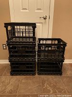 Five black plastic stacking file crates arranged stacked in two columns in front of a door on floor.