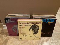 Photo of a large lot of 67 vinyl records in sleeves, showing front covers of some albums such as Lee Greenwood on left and Charley's Best on right with The Very Best of Connie Francis album cover in the center front.