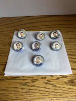 Seven hockey marbles arranged on a white cloth on wooden surface showing player portraits and names.
