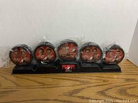 Photo showing five Team Canada hockey pucks sealed in plastic bags, each puck with orange and black player portraits, arranged on black plastic stand with Team Canada logo plaque.