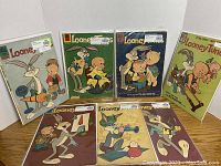 Seven Looney Tunes comics from 1961 laid out on a table, featuring various cover art showing iconic characters such as Bugs Bunny and Elmer Fudd, each in protective plastic sleeves.