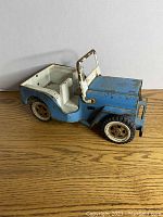 Side angled view of the vintage blue Tonka Jeep showing worn paint, white seats, rust on metal parts, and scuffed tires.