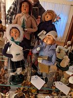 Four Byers Choice caroler figurines grouped together, showing detail of winter clothes and accessories.