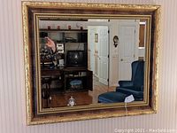 Full shot of the gilt-framed beveled edge mirror hanging on a wall reflecting a room.