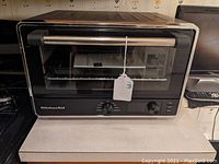 KitchenAid countertop oven front view on countertop with door closed, showing brand logo and control dials.