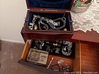 Wooden jewelry box open showing mostly costume jewelry with some pieces marked sterling inside the top compartment and drawer.