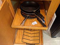 Drawer with several frying pans including early Wagner Number 8 cast iron skillet and other pans with metal handles