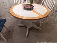 View of round kitchen table with white tile top and wood edges, displays hidden leaf feature by wood strip center.