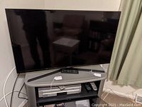 Samsung 40-inch flat screen TV on grey stand with cables, remote control on top