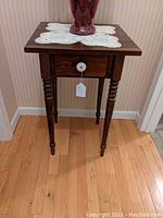 Front view of the small wooden stand with one drawer and porcelain knob, showing the overall size and condition.