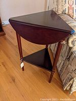 Triangular dark wood drop leaf table closed and positioned beside a patterned couch on hardwood floor.