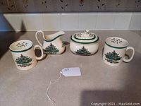 Full set of four items on counter showing creamer, sugar bowl, and two mugs with Christmas tree pattern