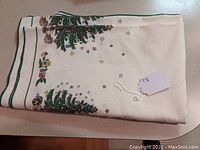 Folded tablecloth showing Christmas tree and star pattern with a small tag attached.