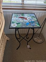 Side view of the stained glass butterfly and floral motif table top and wrought iron base.
