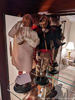 Two Christmas Carol figurines, Scrooge and Bob Cratchit with Tiny Tim, displayed on glass shelf.