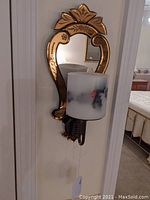 Front view of Venetian glass mirrored wall sconce mounted on wall with frosted glass shade and white pillar candle inside.