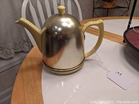 Metallic gold teapot cozy warmer dome cover and base, sitting separately on table
