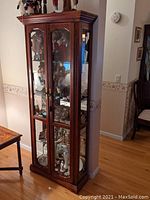 Front view of tall brown walnut curio cabinet with glass front doors and visible collectibles inside.