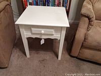 Front and side view of white wooden side table between two sofas on carpet.