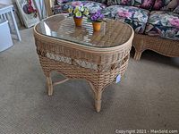 Oval wicker and rattan table with clear glass top, showing tight weaving and curved legs
