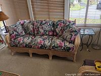 Front view of wicker and rattan sofa with floral cushions showing full seating area and pillows.