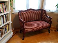 Full view of antique settee couch placed near window and bookshelf, showing wooden frame and striped upholstery.