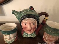 Front view of Sairey Gamp character Toby teapot with two matching character mugs.