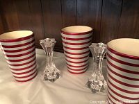 Two ceramic candy cane striped vases with red and white horizontal stripes and two clear crystal cut glass candlesticks shown together on table.