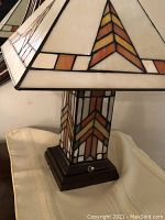 Close-up of stained glass lamp shade and base, showing geometric design with amber, brown, yellow, and white glass panels.