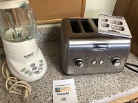 Cuisinart blender and KitchenAid 4-slot toaster on countertop, showing blender base, glass jar, and toaster front with control buttons and dials.