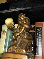 Photo of Darwin statue depicting ape holding human skull with books in the background
