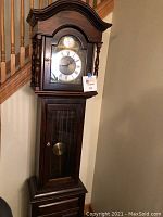 Full view of Ethan Allen grandfather clock showing tall wooden case, glass door, and curved crown molding top.