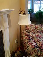 Full view of the brass-tone fleur de lis floor lamp standing next to floral sofa and fireplace.