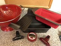 Full view of lot showing red metal colander, silicone-lined bread loaf pan, black loaf pan, Farberware timer, and two KitchenAid clips