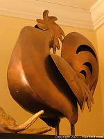 Side view of the copper rooster statue showing the shaped copper metal and curved design details.
