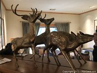 Three metal deer sculptures on table with window background, showing size and detail
