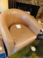 Front angle view of tan vinyl club chair showing rounded backrest and armrests with cushioned seat.