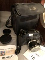 Olympus SLR camera with lens attached, lens caps, and carrying case in background.