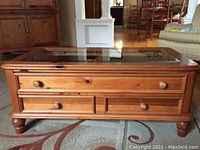 Pine coffee table with glass inset top, four drawers with wooden knobs, and turned legs placed on a carpet in a living room setting.