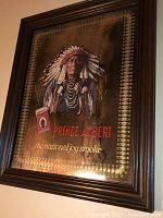 Front angled view of framed print showing Native American man and Prince Albert tobacco package with gold decorative border.
