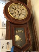 Full view of the clock showing round face with Roman numerals and lower glass door labeled 'REGULATOR' revealing pendulum inside.