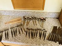 Full view of silverware spread out including knives, forks, spoons, and mini cutting board on countertop