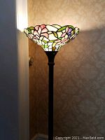 Close-up front view of lamp showing stained glass floral shade lit with soft warm light, dark metal stand and base.