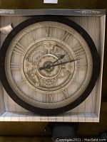 Full view of the large circular wall clock with Roman numerals and mechanical gear design, shown in an open box.