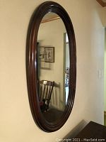 Front and angled views of the large oval mirror mounted on a wall, showing the dark wood frame and reflective glass.