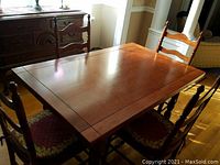 Photo of vintage wooden dining table and four chairs around it with wooden floor and sideboard background.