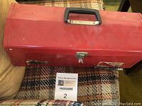 Closed red metal toolbox with handle, showing front and top sides with latch.