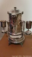 Front view of entire tilting pitcher set showing body, stand and two goblets