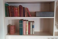 Shelf view showing two rows of books; top left cluster of assorted cloth-bound volumes and top right large grey dictionary.